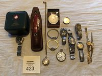 All watches and items laid out on cloth background showing the full lot including Swiss Military wristwatch box and Swiss Army multi-tool.