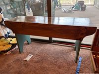 Front view of wooden bench with natural wood top and greenish-blue painted legs.