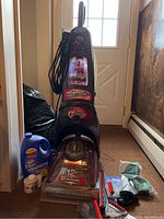 Full view of the Bissell ProHeat Select 2X vacuum cleaner with accessory brushes, cleaning liquid, and manual on the floor beside it.