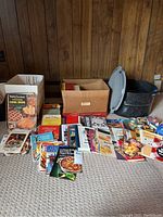 Overview of canning pot, lids, bands, multiple vintage and newer cookbooks, and cardboard boxes in background.