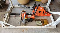 Two Echo chainsaws shown on ground next to large planter; includes spare chain in plastic packaging