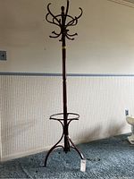 Full view of tall wooden coat rack standing on carpeted floor, showing overall height and design