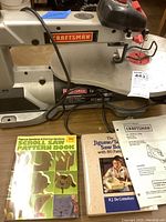 Photo of Craftsman 16" variable speed scroll saw on table with operator's manual and two pattern books placed in front.