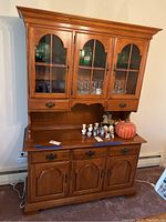 View of closed wooden two-piece hutch with glass inset cabinet doors on top and wooden cabinet doors below, along with drawers.