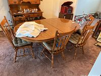 Dining table with two leaves inserted surrounded by four wood chairs with cushions and table cloth draped