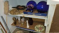 Shelf with two blue glass gazing balls, Pennsylvania Dutch wooden plaque, plastic butterfly decor, multiple vases, and a clock.