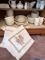 Photo of the entire set stored inside a cabinet showing stacked dinner plates, bowls, cups, saucers, and various serving pieces along with the table runners.