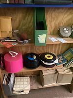 Shelf showing multiple stacks of 45 RPM vinyl records, pink lighted View-Master device, children's books and other storage boxes.