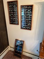 Two wood framed glass display cases on wall and one on floor showing the souvenir spoon collections.