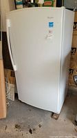 Front view of the white Whirlpool upright freezer, showing the door, handle, and brand stickers.