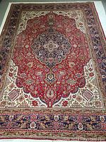 Full view of rug laid flat showing red central field with medallion and floral border
