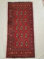 Full view of the rectangular rug showing geometric and tribal motifs, red base color, bordered with intricate smaller geometric bands, fringed ends.