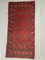 Full view of the hand knotted Persian Turkman wool rug with red background and geometric patterns, showing the complete rug including fringes.