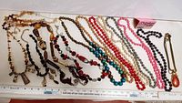 Wide view of 13 assorted necklaces laid out, showing variety in colors, bead types, and lengths, includes beads, stones, glass, and metal accents.