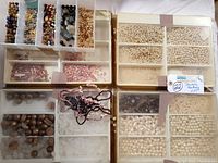 Photo showing 4 trays with various beads and jewelry making supplies including pearl beads, wooden beads, black and gold-tone elements.