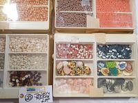 Top view of multiple trays filled with vintage cameo beads, resin cabochons with images, and small beads in various colors.