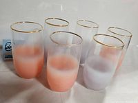 Six mid-century modern style drinking glasses showing a blend of peach orange and frosted glass with gold rims arranged in two rows.