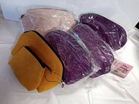 Five leather clutches and coin purses in plastic packaging, showing various colors including pink, purple, and gold brown.