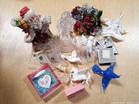 Photo shows an assortment of vintage Christmas and holiday decorations including a Santa Claus figurine, white fabric angel, crystal nutcracker, pine greenery and various glass and ceramic ornaments including white horse figurines and blue glass bird.