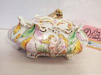 Angled side view of vintage ELPA pottery lidded dish featuring hand-painted cherubs, gold gilding details and floral motifs.