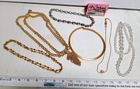 View of all five necklaces laid out on a white background with measurement scale beneath them.