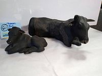 Photo showing the two sculptures side by side on a white surface, the larger bull and smaller calf clearly visible with patterned tribal engravings.
