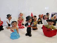 Front angled view of the 14 mini Spanish mud clay people arranged in rows showing diverse characters including the bride, groom, musicians, and villagers, highlighting their colorful hand-painted details and size scale.