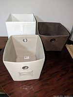 Photo showing three fabric storage bins (white, dark brown, and beige) on a wooden surface.