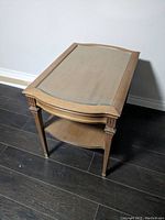 Side and top view of a wooden end table with inset glass top and lower shelf, showing table legs and decorative accents.