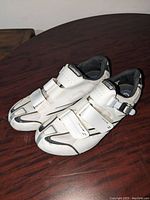 Pair of white Shimano cycling shoes with three adjustable straps and buckle, showing light use marks on toe and sides.