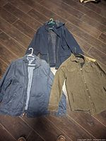 Three men's jackets on hangers viewed from front showing colors and materials.