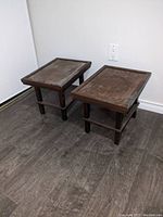 Pair of small wooden tables with worn surfaces on wood floor against white wall