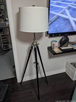 Full view of the tripod style floor lamp showing black metal tripod legs and white drum lampshade.