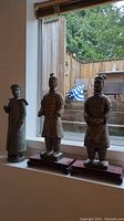 Three Chinese sculptures displayed on a windowsill with outdoor background, showing scale and placement.