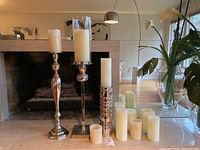 Set of three decorative metal candle stands with pillar candles in front of fireplace