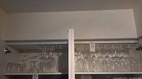 Cabinet interior showing an assortment of clear glass stemware including wine glasses hung upside down on racks.