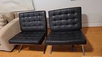 Front view of both black tufted leather Barcelona chairs with stainless steel frames