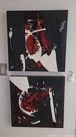 Two matching original abstract oil paintings shown hung on the wall, both square shaped. Dominant black background with red and white abstract shapes.