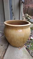 Side view of large beige ceramic planter pot sitting outside near stone garden and concrete steps.