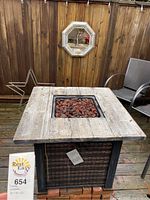 Front view of propane fireplace table showing wooden top, woven sides, and lava rocks in fire pit