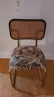 Front view of chair showing brass frame, cane backrest, jungle themed upholstery on seat depicting a tiger and lion amid leaves.