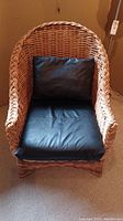 Front view of wicker chair with black leather seat and back cushions.