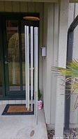 Full view of the windchime hanging in an outdoor covered entryway with door and siding visible