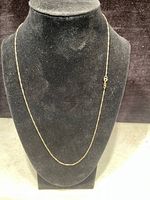 Full view of thin gold chain displayed on black mannequin bust, showing overall length and color.