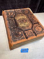 Top angle view of the antique Bible showing the worn black leather cover with embossed designs and gold leaf title.