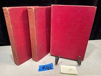 Three red cloth hardcover books from 1887, standing and arranged side by side displaying spines and fronts with embossed designs.