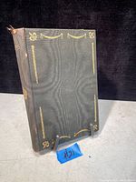 Front cover of the antique book showing dark cloth cover with gold leaf decorative motifs and some wear on spine edges.