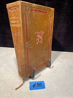 Antique leather-bound hardcover book standing on a display stand. The book spine shows the title 'The Works of Shakespeare' with gold and red embossing.