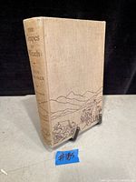 Front cover and spine of the book showing beige cloth binding with black printed illustration and text