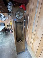 Full view of the tall oak grandfather clock showing the detailed wood case and overall height in a workshop setting.